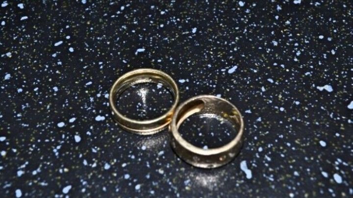 Zwei goldene Eheringe liegen auf einer gl&auml;nzenden, schwarz gepunkteten Oberfl&auml;che und symbolisieren Bruchgold und Altschmuck.