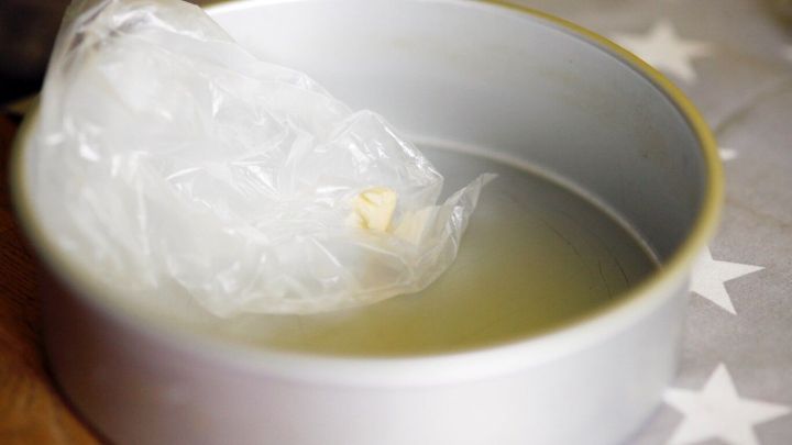 Eine runde Backform ist mit &Ouml;l gef&uuml;llt, w&auml;hrend ein St&uuml;ck Plastikfolie darin liegt, bereit zum Einfetten.