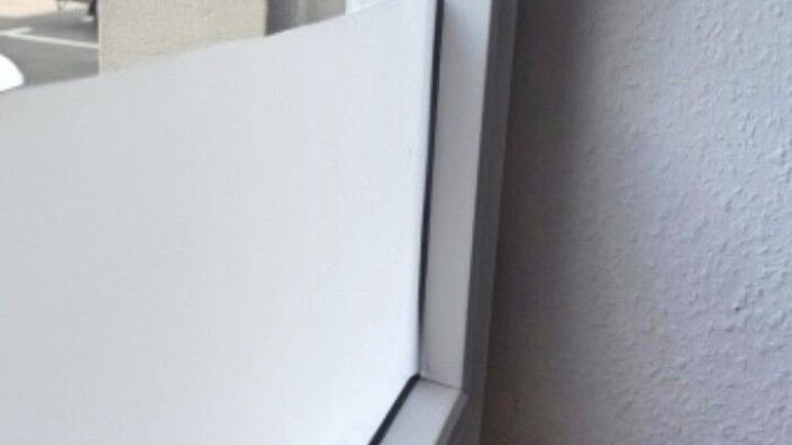 Eine selbstklebende Glasfolie wird an einem Fenster angebracht, w&auml;hrend das Zimmer hell erleuchtet ist und ein Kabel sichtbar ist.