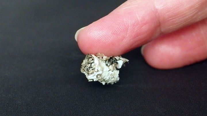 Eine Hand h&auml;lt Zigarettenasche, die langsam aufgehoben wird, auf einer dunklen Unterlage.