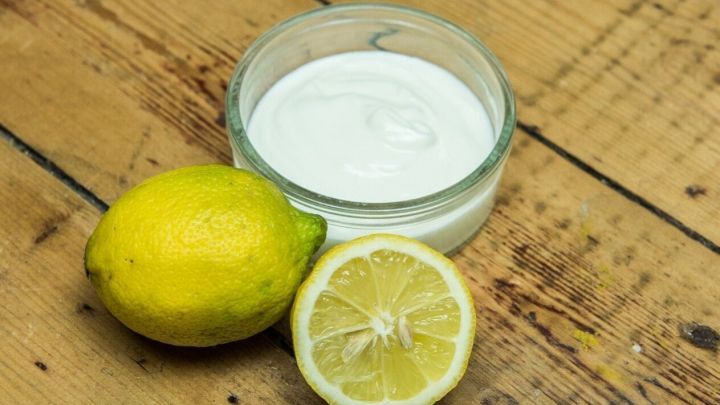 Eine Schale mit Gesichtspflege steht auf einem Holztisch, daneben liegen eine ganze und eine halbe Zitrone.