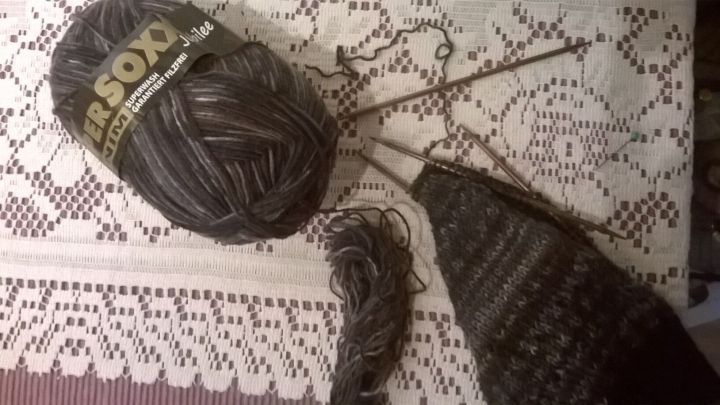 Ein Wollkn&auml;uel liegt auf einer Spitzendecke, w&auml;hrend Stricknadeln ein begonnenes Projekt in Schwarz voranbringen.