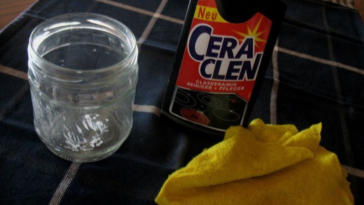 Ein leeres Glas steht neben einer Flasche mit CeraClen und einem gelben Tuch, ideal zum Entfernen von Etiketten-Kleberresten.
