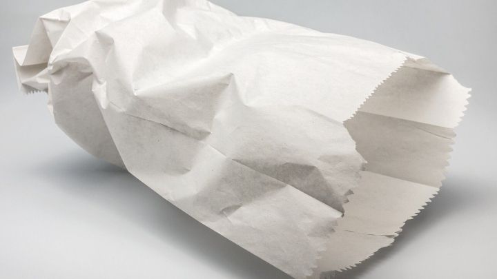 Ein zusammengekn&uuml;llter, wei&szlig;er Papierbeutel liegt auf einem neutralen Hintergrund und wird zur sauberen Entsorgung von Tampons und Binden verwendet.