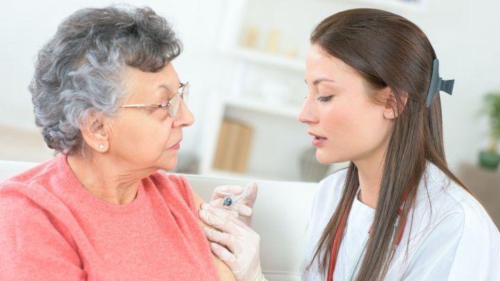Eine Krankenschwester injiziert einer &auml;lteren Frau die Grippeimpfung in einer hellen, modernen Praxis.