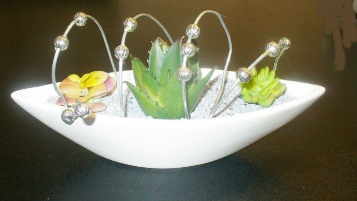 Ein moderner Blumenschmuck besteht aus Sukkulenten in einer eleganten Schale, umgeben von Drahtverzierungen.