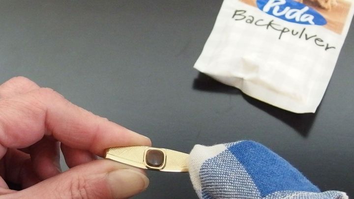Ein Goldring wird mit einem Tuch und Backpulver gereinigt. Im Hintergrund befindet sich eine Packung Backpulver.