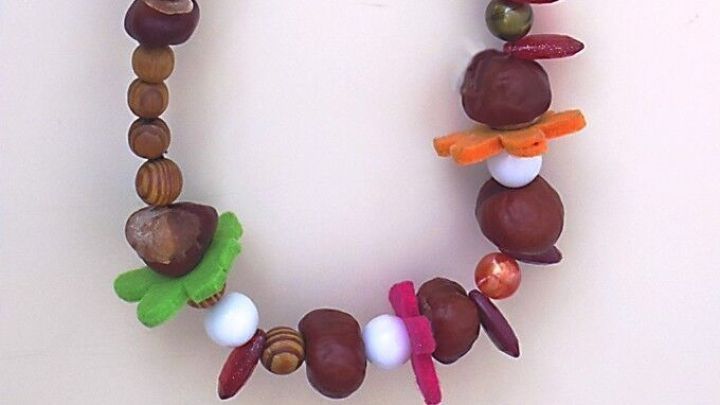 Ein T&uuml;rkranz mit Perlen und Kastanien h&auml;ngt dekorativ an einer Wand, umgeben von fr&ouml;hlichen Farben und herbstlichem Charme.