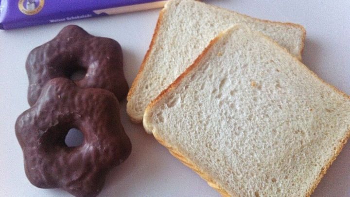 Zwei Donuts und zwei Scheiben Brot liegen auf einem Tisch, begleitet von einer violetten Verpackung im Hintergrund.