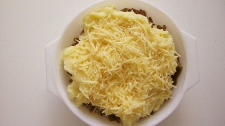 Der Bauernauflauf wird in einer wei&szlig;en Sch&uuml;ssel pr&auml;sentiert, mit einer Schicht aus geriebenem K&auml;se, die auf einer Kartoffelmasse liegt.