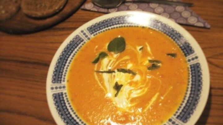 Eine cremige Quitten-Cremesuppe mit H&uuml;hnerfleisch ist dekorativ in einer Schale angerichtet, umgeben von Kn&auml;ckebrot, auf einem Holztisch.