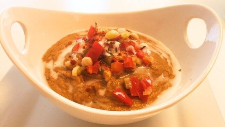 Eine cremige Linsensuppe mit Kokosmilch, garniert mit frischen Tomaten und N&uuml;ssen, in einer wei&szlig;en Sch&uuml;ssel serviert.