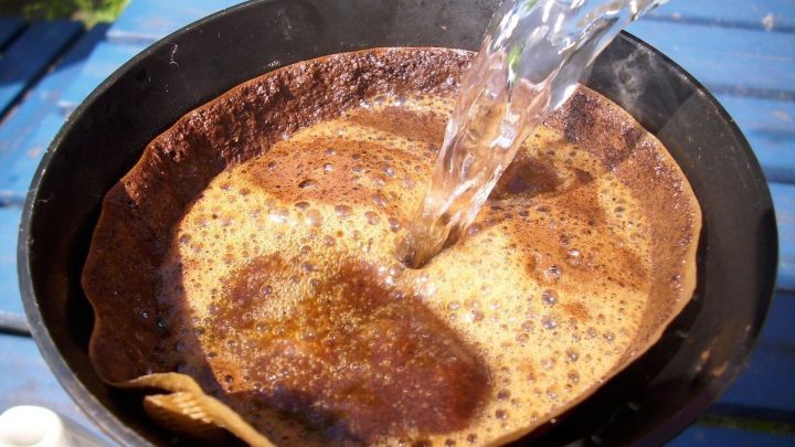 Ein Kaffeefilter wird mit hei&szlig;em Wasser bef&uuml;llt, w&auml;hrend im Hintergrund eine blaue Oberfl&auml;che sichtbar ist.