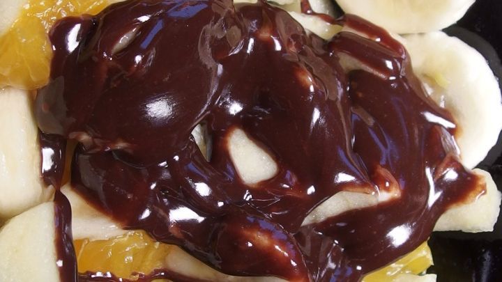 Ein Teller mit frischen Bananen und Orangen, &uuml;berzogen mit dickem Schokoladensirup, zeigt einen k&ouml;stlichen Dessertgenuss.
