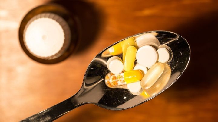 Eine L&ouml;ffel mit verschiedenen Kombi-Pr&auml;paraten gegen Erk&auml;ltung liegt auf einem Holztisch neben einer Flasche.