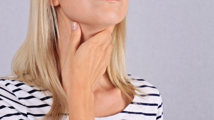 Eine Frau h&auml;lt sich den Hals, m&ouml;glicherweise wegen eines verschluckten Gegenstands, in einem neutralen Raum.