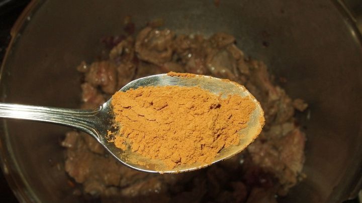 Ein L&ouml;ffel Zimtpulver schwebt &uuml;ber einem topf mit gebratenem Fleisch, das f&uuml;r Weihnachtsgulasch vorbereitet wird.
