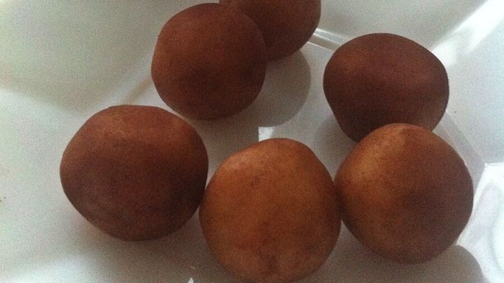 Runde Marzipankartoffeln liegen auf einem wei&szlig;en Teller, w&auml;hrend ein Glas Backkakao im Hintergrund steht.