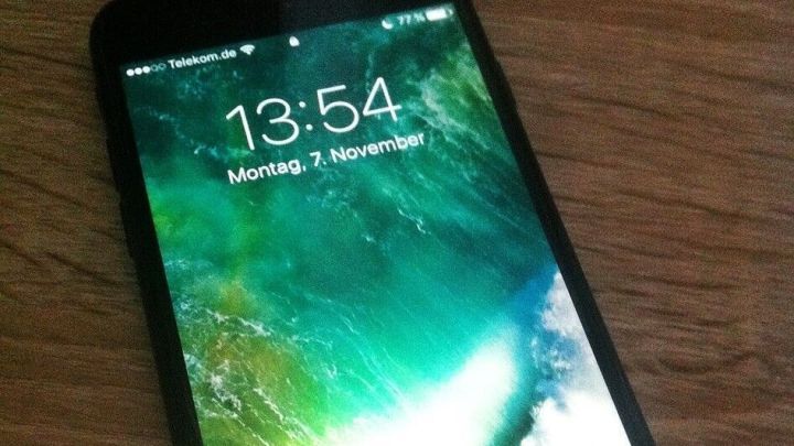 Ein Smartphone liegt auf einem Holztisch und zeigt die Uhrzeit 13:54 sowie das Datum auf dem Bildschirm.