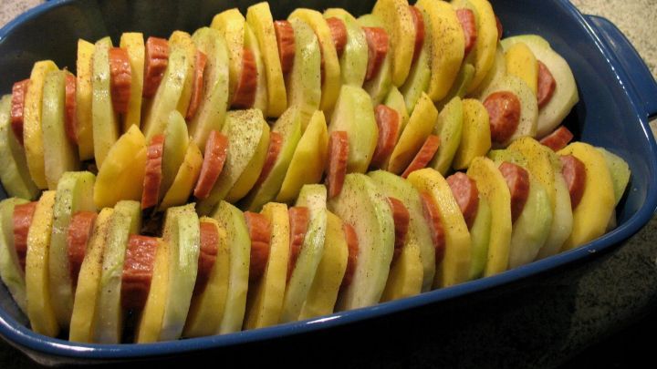 Ein schichtweise angeordnetes Kohlrabi-Kartoffel-Gratin liegt in einer blauen Auflaufform auf einer Arbeitsplatte.