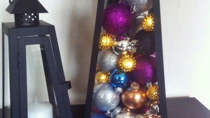 Eine schwarze Laterne mit bunten Weihnachtskugeln steht neben einer weiteren Laterne mit einer Kerze, festliche Dekoration.