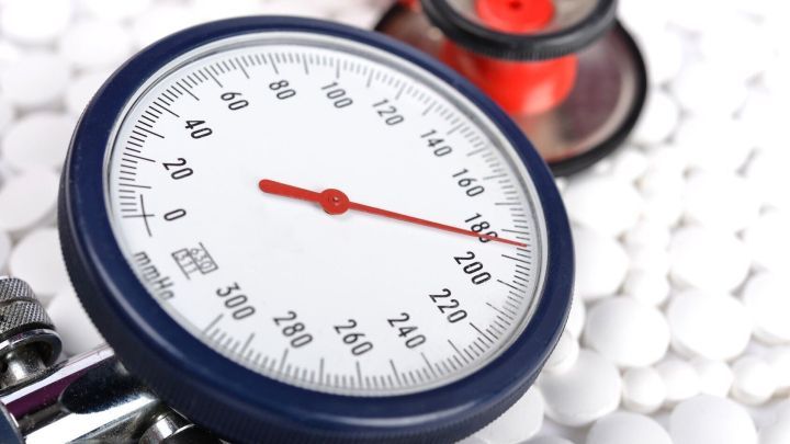 Ein Blutdruckmessger&auml;t zeigt einen hohen Wert an, w&auml;hrend wei&szlig;e Tabletten im Hintergrund f&uuml;r die Behandlung von Bluthochdruck liegen.