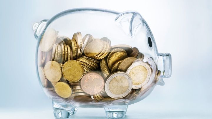 Ein transparentes Sparschwein mit M&uuml;nzen drin steht auf einer hellen Fl&auml;che, symbolisiert das Sparen beim Rauchen aufh&ouml;ren.