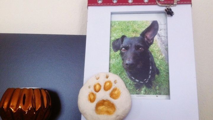 Ein Salzteig-Pfotenabdruck liegt neben einem gerahmten Foto eines Hundes auf einem Regal, umgeben von Dekor.