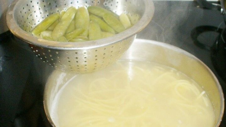 Im Topf k&ouml;cheln Nudeln, w&auml;hrend im Sieb dar&uuml;ber Gem&uuml;se dampft, auf einer Herdplatte in einer modernen K&uuml;che.