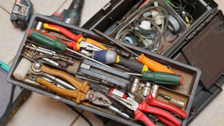Werkzeugkasten voller Handwerkszeug liegt offen auf dem Boden. Enthalten sind Schraubendreher, Zangen und Kleinteile.