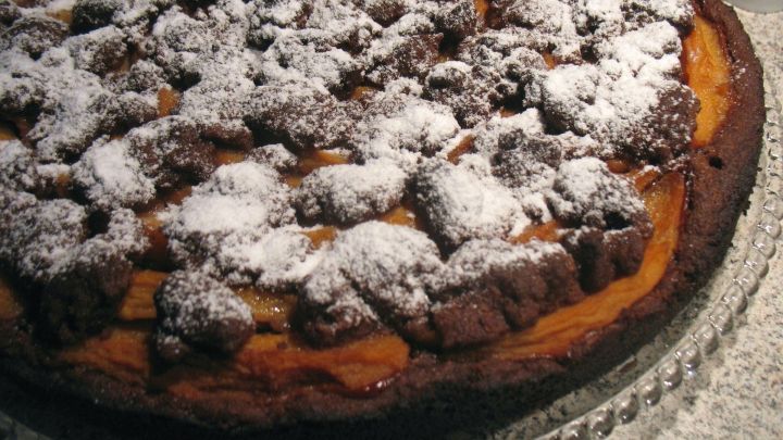 Eine saftige Schoko-Quitten-Torte liegt auf einer eleganten Platte, mit knusprigen Kakaostreuseln und Puderzucker bestreut.