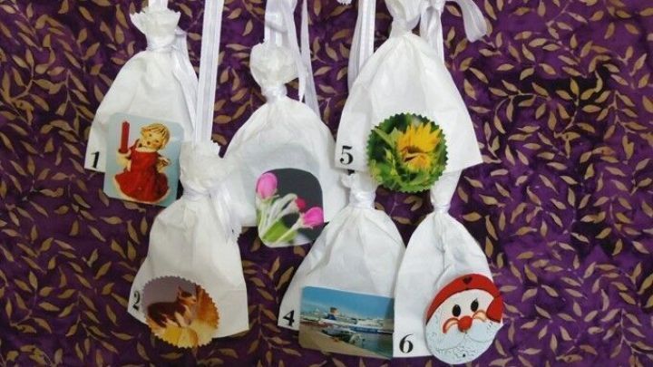 Eine Reihe von wei&szlig;en S&auml;ckchen mit dekorativen Bildern h&auml;ngt an einem Holzstab, bereit f&uuml;r einen 6-Tage-Adventskalender.