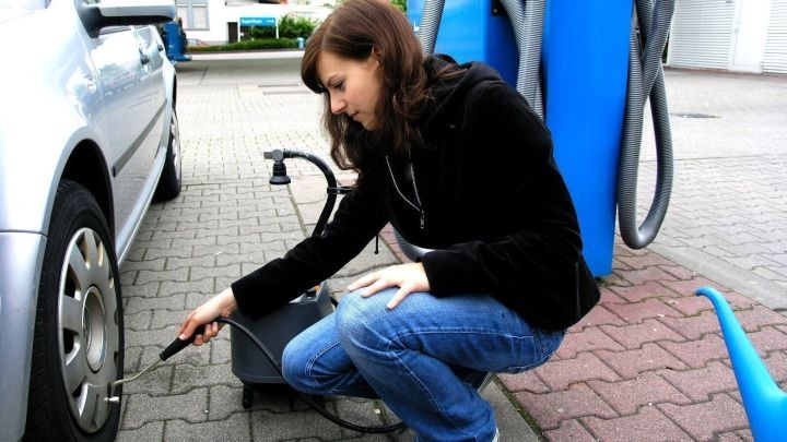 Eine Frau pr&uuml;ft die Autoreifen an einem Reifenf&uuml;llautomaten in einer Tankstelle, um den Reifendruck zu kontrollieren.