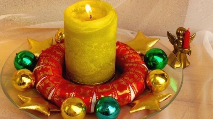 Ein roter Kranz umwickelt mit bunten Kugeln und einem gelben Licht, das in einem festlichen Umfeld leuchtet.