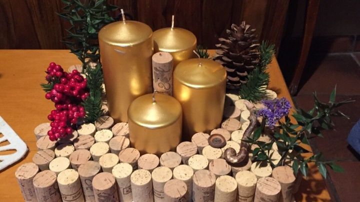 Ein Adventskranz aus Korken mit goldenen Kerzen, umgeben von Tannenzapfen und roten Beeren auf einem Holztisch.