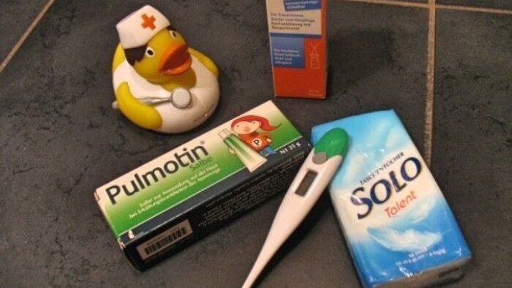 Eine Gummiente mit Krankenpflegerhut liegt neben Medikamenten, einem Fieberthermometer und einer Verpackung f&uuml;r Lutschtabletten.