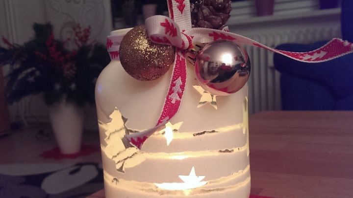 Ein dekoratives Windlicht leuchtet sanft, umgeben von festlichen Sternen und einer roten Unterlage, ideal f&uuml;r die Adventszeit.