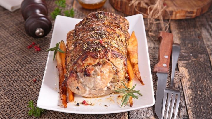 Ein saftiger Braten liegt auf einem wei&szlig;en Teller, umgeben von goldbraunen Kartoffeln in einer rustikalen Umgebung.