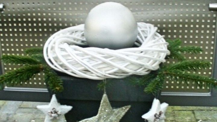 Eine silberne Solarkugel sitzt in einem Topf, umgeben von Dekorationen und Tannenzweigen, vor einer modernen Wand.