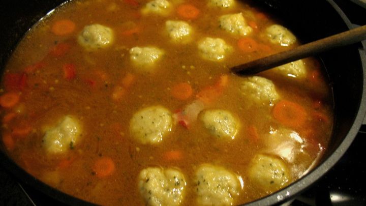 Ein gro&szlig;er Topf Winter-Eintopf mit Hackfleisch und Semmelkn&ouml;deln kocht auf dem Herd, umgeben von buntem Gem&uuml;se.