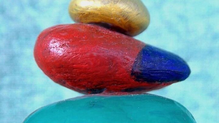 Eine bunte Steinpyramide steht auf einer glatten Oberfl&auml;che, umgeben von einem sanften, einfarbigen Hintergrund.