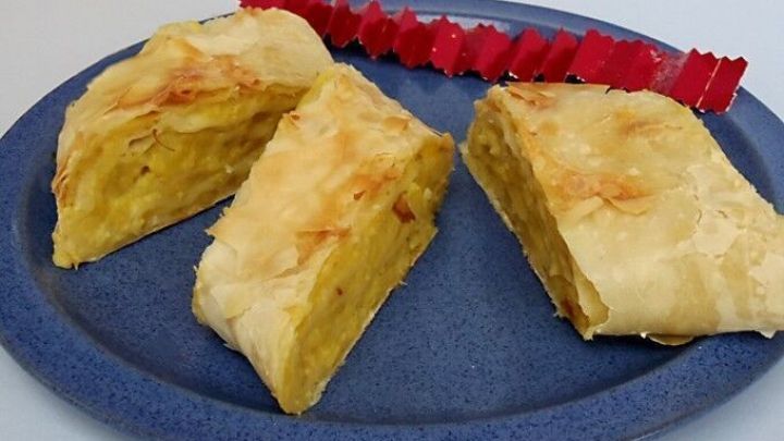 Drei goldbraune St&uuml;cke Kartoffelstrudel liegen auf einem blauen Teller, begleitet von rotem Dekor, bereit zum Genie&szlig;en.