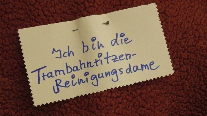 Ein handgeschriebener Zettel liegt auf rotem Stoff und k&uuml;ndigt an: "Ich bin die Trambahnritzen-Reinigungsdame."