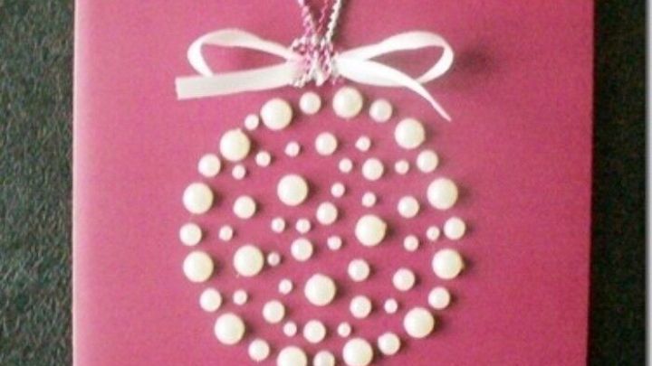 Eine festliche Weihnachtskarte mit Perlen ist auf einem pinken Hintergrund platziert und zeigt eine elegante, perlenbesetzte Dekoration.