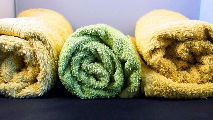 Drei handgerollte Handt&uuml;cher in Gelb und Gr&uuml;n liegen ordentlich nebeneinander auf einer dunklen Oberfl&auml;che.