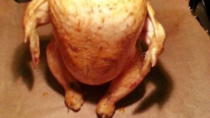 Ein goldbraun gebratenes H&uuml;hnchen steht auf Backpapier in einem Ofen, bereit, gleichm&auml;&szlig;ig gegart zu werden.