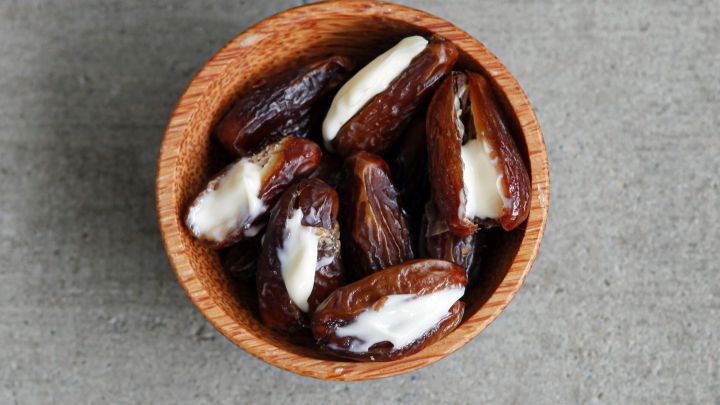 Datteln sind in einer Holzsch&uuml;ssel mit Creme gef&uuml;llt, auf einer grauen Oberfl&auml;che arrangiert, bereit zum Genie&szlig;en.