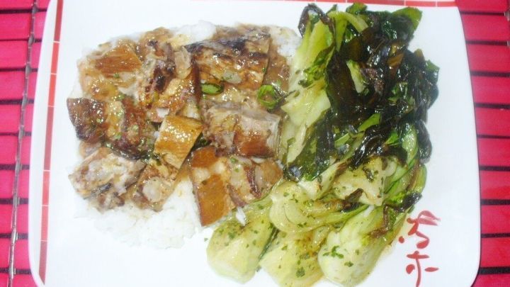 S&uuml;&szlig;saure Rippchen liegen auf Duftreis, daneben geschmorter Pak Choi auf einem wei&szlig;en Teller vor rotem Hintergrund.