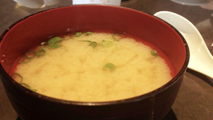 Eine Sch&uuml;ssel Suppe ist sichtbar, mit einem milden Aussehen und Kr&auml;utern oben. Sie befindet sich auf einem Tisch, umgeben von Geschirr.