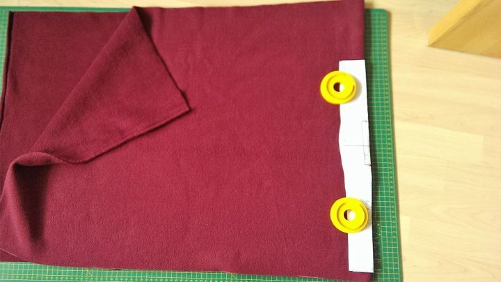 Ein rotes St&uuml;ck Stoff liegt auf einem Schneidemat, w&auml;hrend zwei gelbe Schneiderollen und ein Lineal zum Zuschneiden bereitgestellt sind.